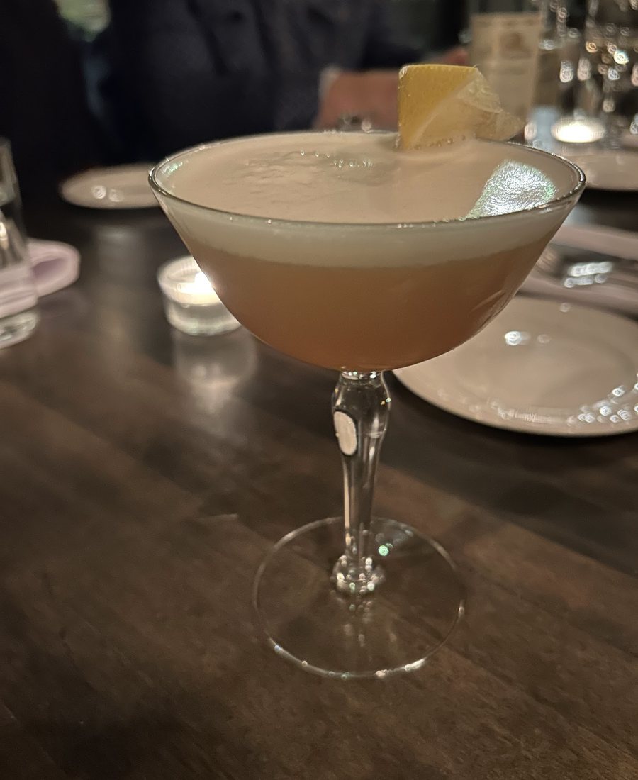 Un cocktail servi dans un verre à pied, mousse sur le dessus et zeste de citron
