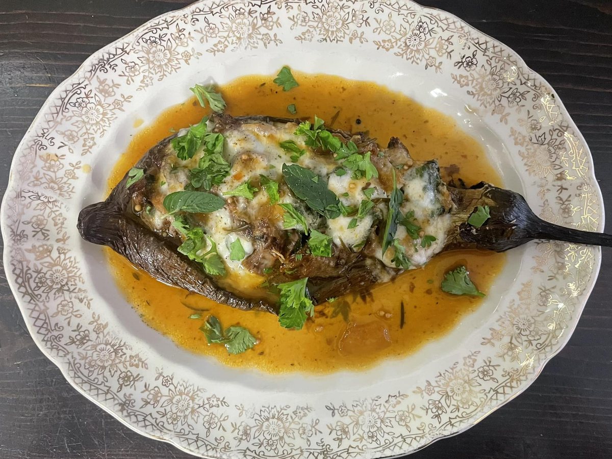 Un plat gratiné servi dans un grand plat ovale ancien, avec des herbes fraîches