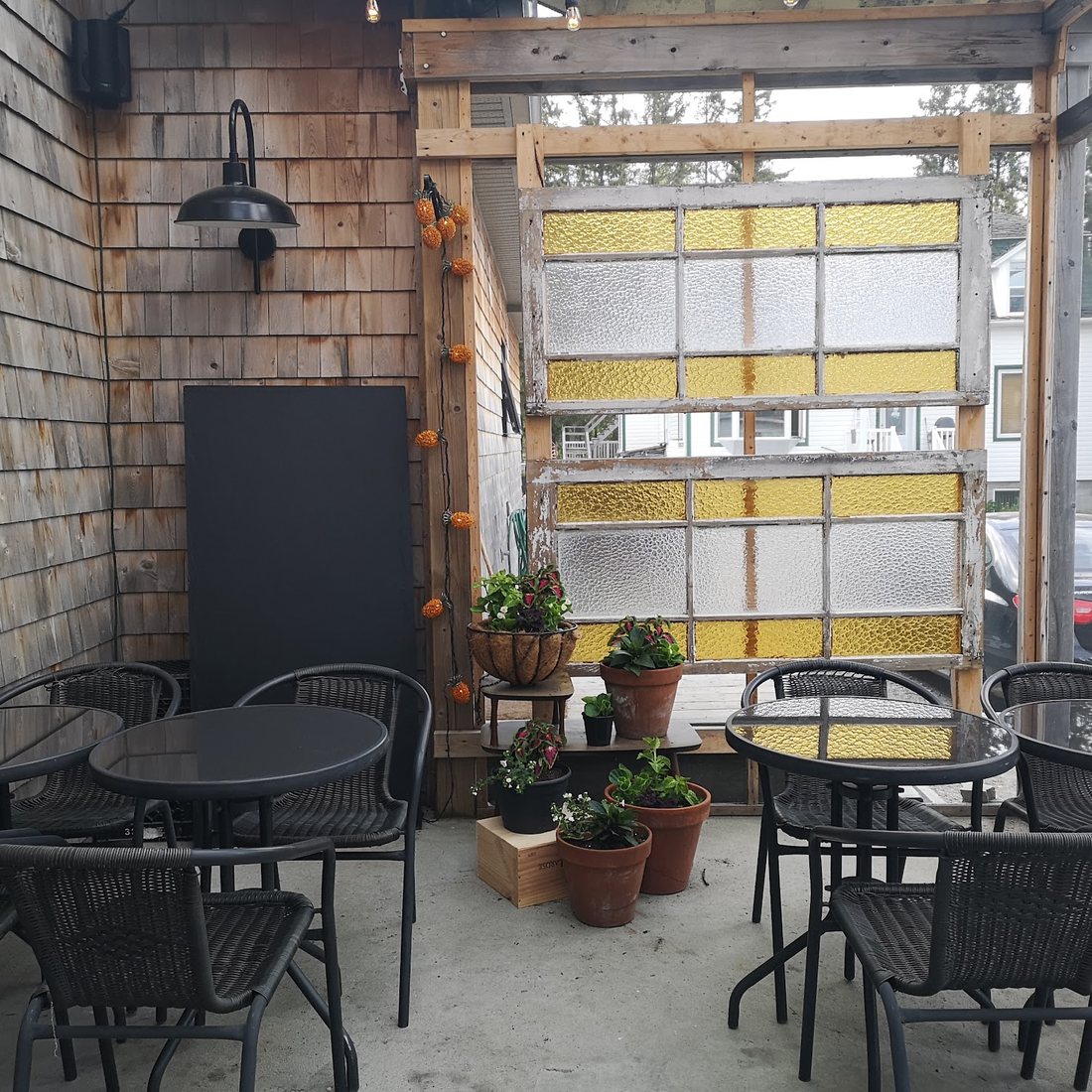 La terrasse couverte, ses tables de bistro noires et ses pots de fleurs, sous une porte de garage vitrée