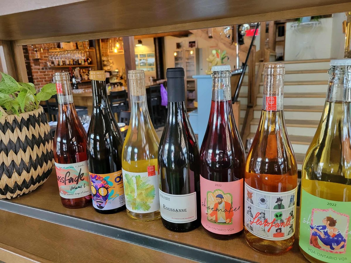 Une rangée de bouteilles de vin nature aux étiquettes illustrées, sur le comptoir du bar